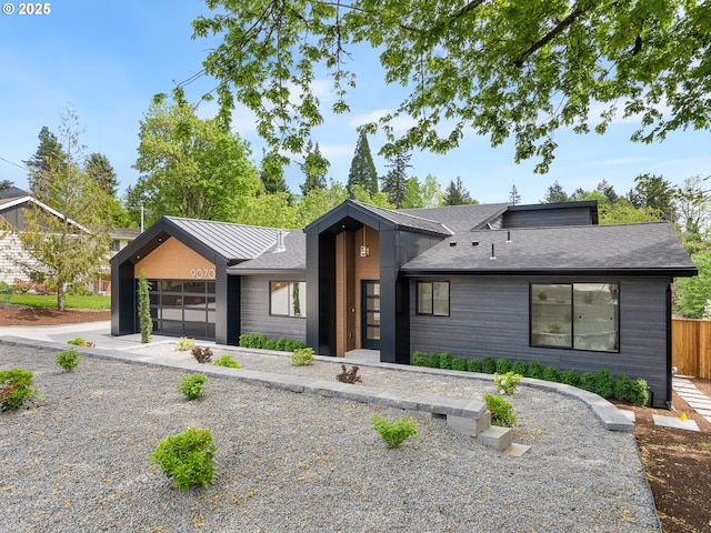 view of front facade with a shingled roof, a garage, and fence