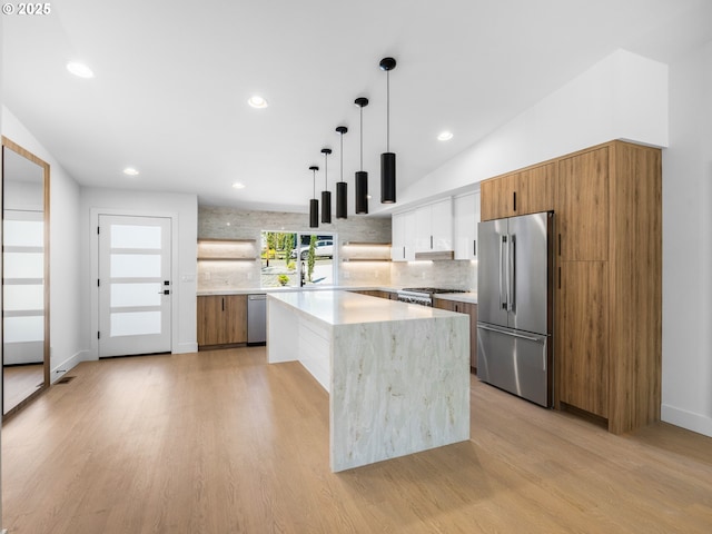 kitchen featuring decorative light fixtures, brown cabinetry, light wood finished floors, stainless steel appliances, and tasteful backsplash