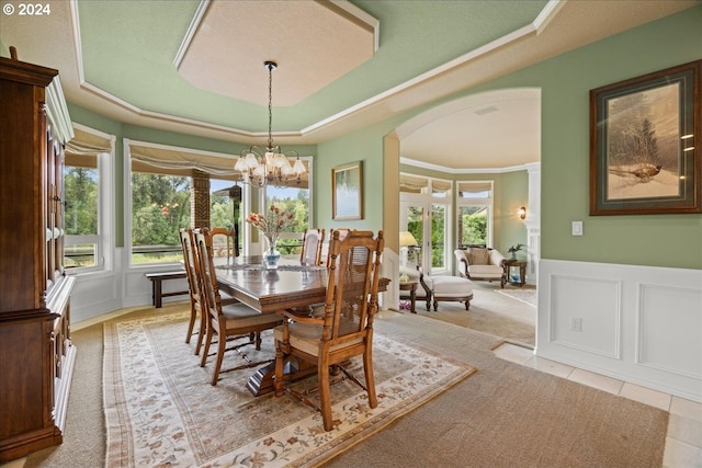 dining space featuring arched walkways, a chandelier, a decorative wall, a raised ceiling, and wainscoting