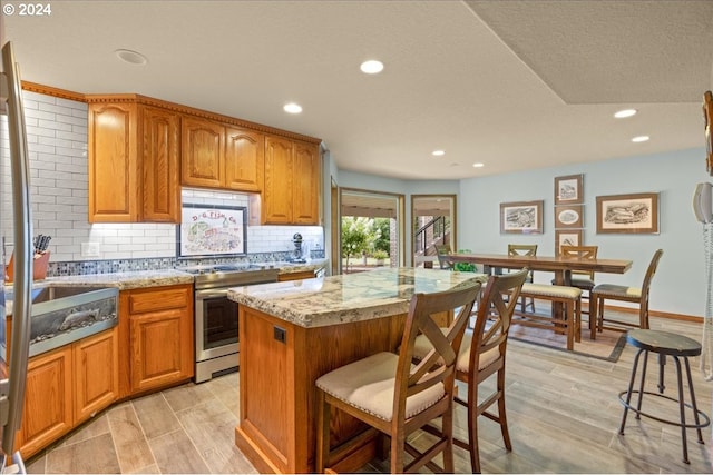 kitchen with stainless steel electric range, recessed lighting, backsplash, light stone counters, and a breakfast bar area