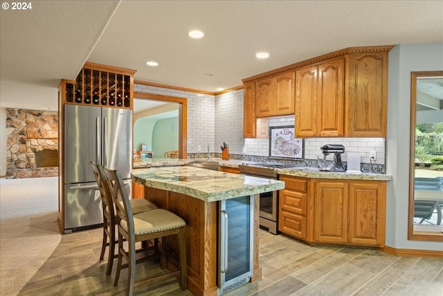 kitchen with appliances with stainless steel finishes, wine cooler, light wood-type flooring, backsplash, and recessed lighting