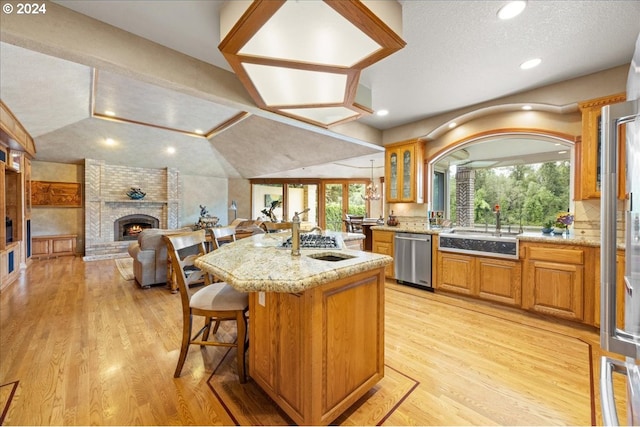 kitchen featuring appliances with stainless steel finishes, a sink, open floor plan, a brick fireplace, and an island with sink