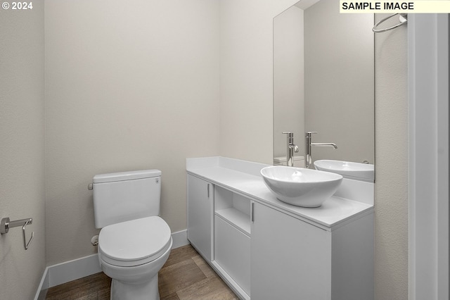 half bath featuring vanity, wood finished floors, toilet, and baseboards