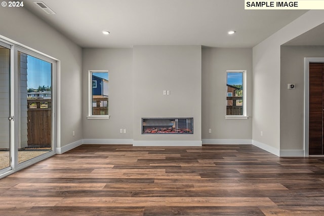 unfurnished living room with a glass covered fireplace, dark wood-style flooring, visible vents, and baseboards