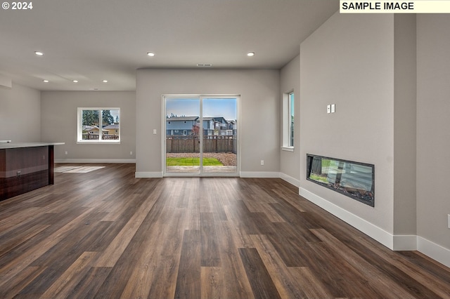 unfurnished living room featuring dark wood-style floors, baseboards, and a glass covered fireplace