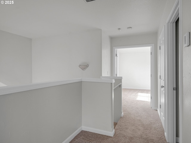 hallway featuring an upstairs landing, baseboards, and light colored carpet