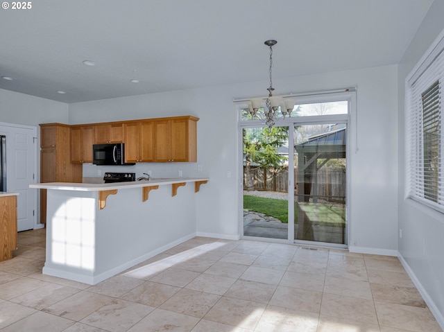 kitchen featuring black microwave, a breakfast bar, light countertops, brown cabinetry, and decorative light fixtures