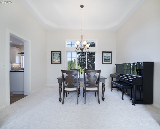 dining room with a tray ceiling, a notable chandelier, light colored carpet, and baseboards