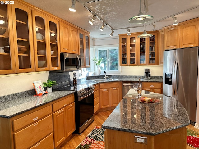 kitchen with a center island with sink, a sink, stainless steel appliances, glass insert cabinets, and light wood-type flooring