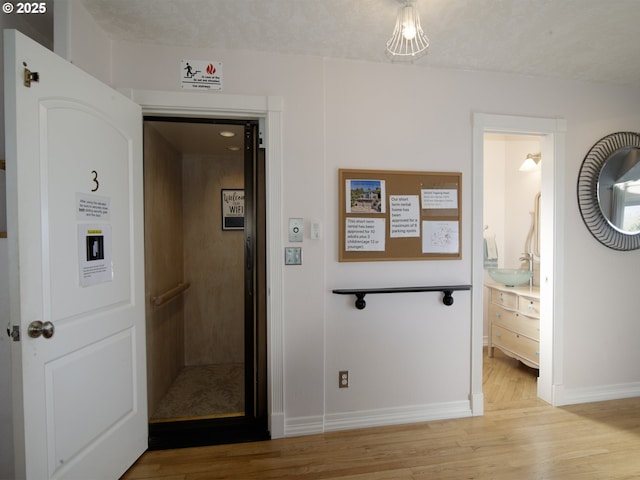 hall with a sink, baseboards, elevator, and light wood-style flooring