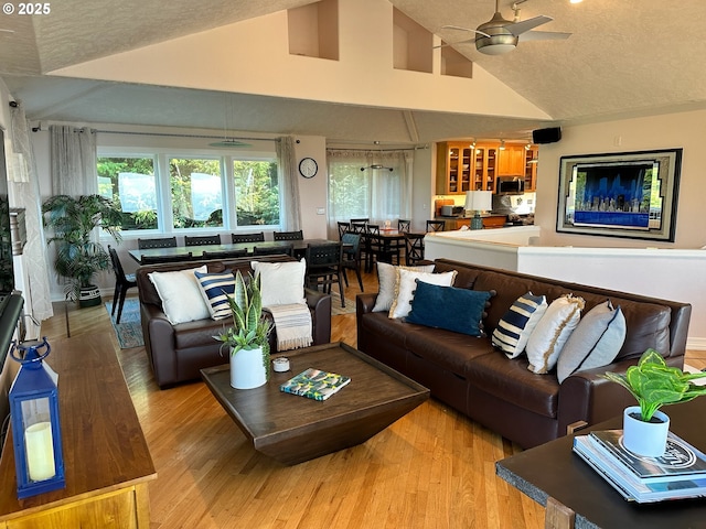 living room featuring a textured ceiling, high vaulted ceiling, light wood finished floors, and ceiling fan