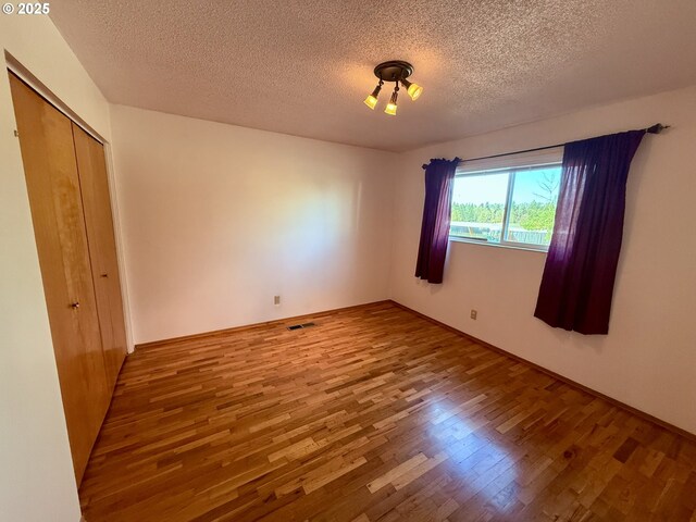 unfurnished bedroom featuring a textured ceiling, a closet, and hardwood / wood-style floors