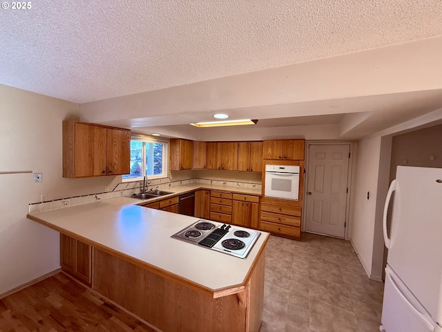 kitchen with sink, white appliances, a textured ceiling, and kitchen peninsula