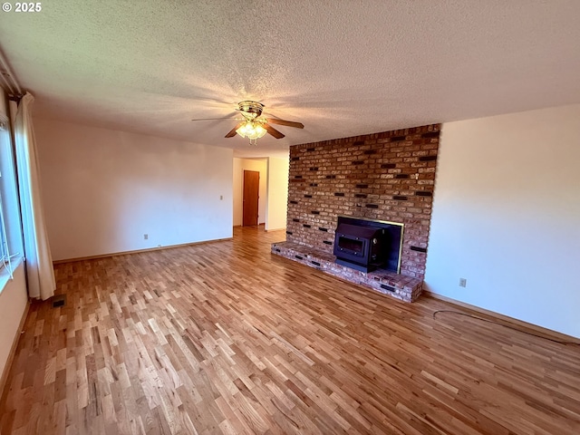 unfurnished living room with a wood stove, light hardwood / wood-style flooring, ceiling fan, and a textured ceiling