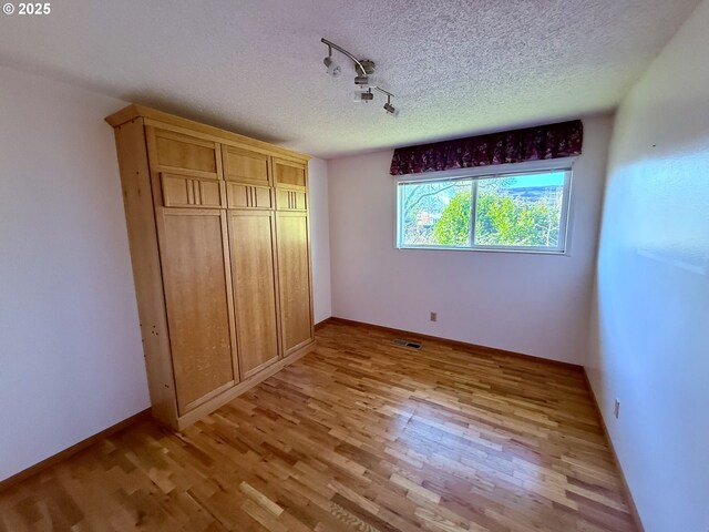 unfurnished bedroom featuring rail lighting, light hardwood / wood-style floors, a textured ceiling, and a closet