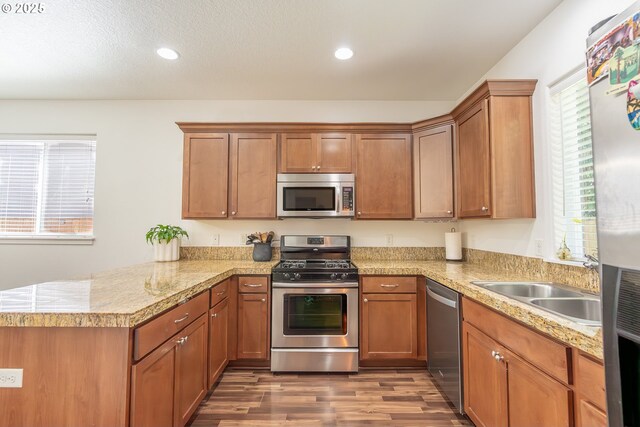5065 SW 207th Pl, Beaverton, OR 97078 - kitchen featuring stainless steel appliances, a peninsula, wood finished floors, brown cabinetry, and a sink