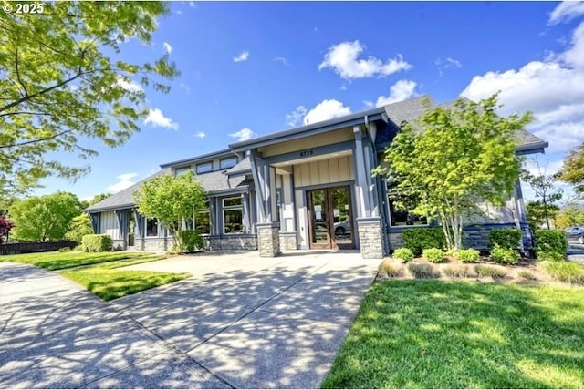 view of front of property with stone siding, french doors, board and batten siding, a front yard, and driveway