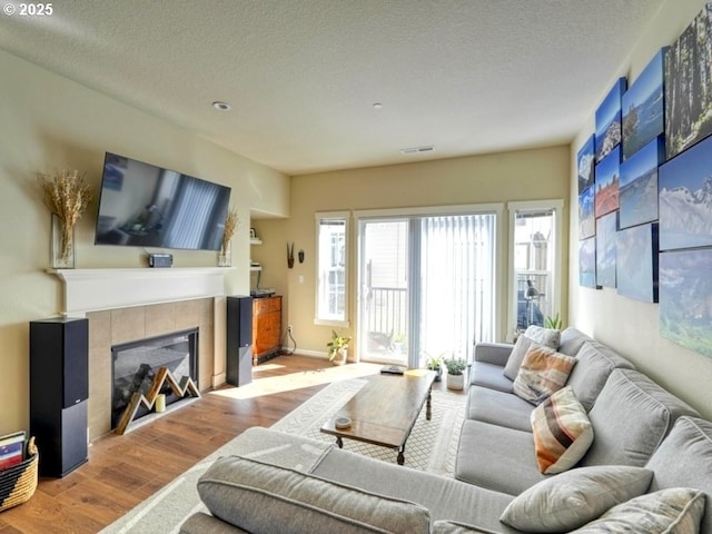 living area with a tile fireplace, visible vents, a textured ceiling, and wood finished floors