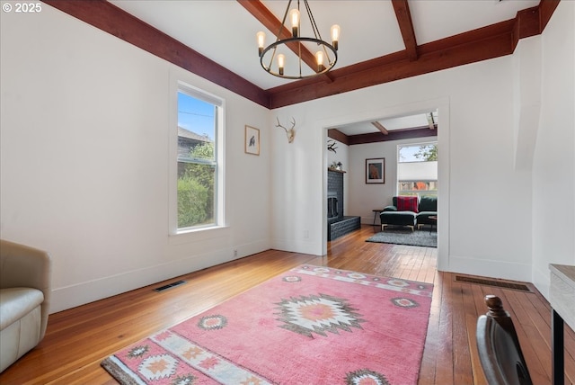 living area featuring a fireplace, visible vents, hardwood / wood-style floors, beamed ceiling, and baseboards