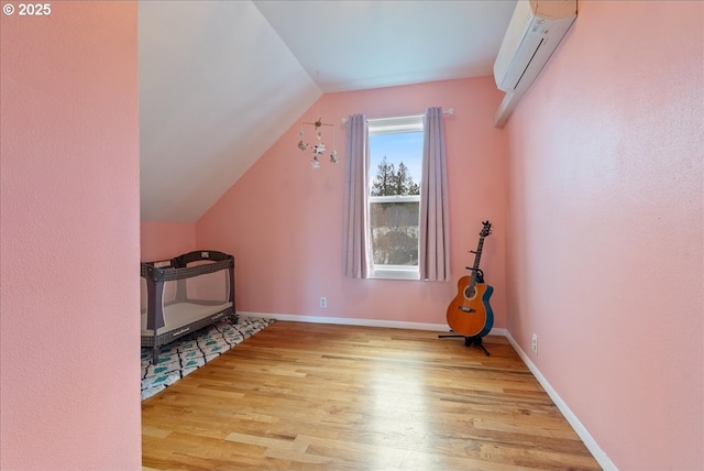 bonus room featuring lofted ceiling, a wall unit AC, wood finished floors, and baseboards