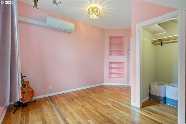 unfurnished bedroom featuring a wall unit AC, wood finished floors, and baseboards