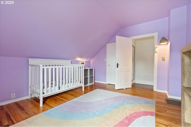 bedroom with lofted ceiling, wood finished floors, visible vents, and baseboards