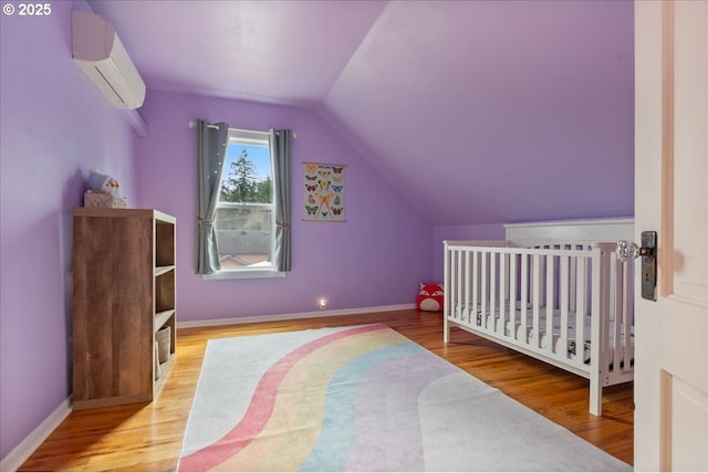 bedroom featuring lofted ceiling, baseboards, wood finished floors, and a wall mounted air conditioner