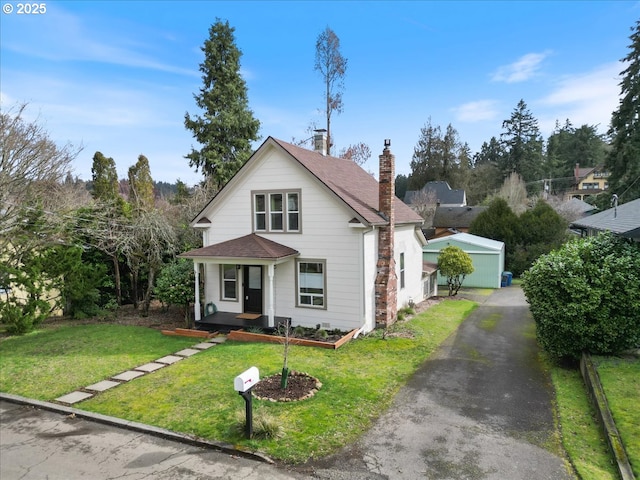 view of front facade with driveway, a chimney, an outbuilding, a porch, and a front yard