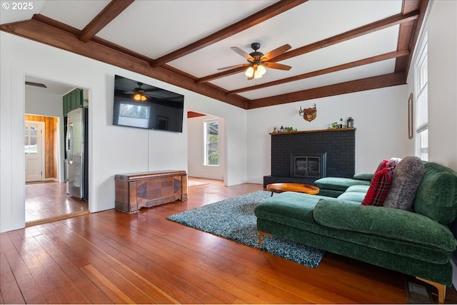 living room with wood-type flooring, a fireplace, a ceiling fan, and beamed ceiling