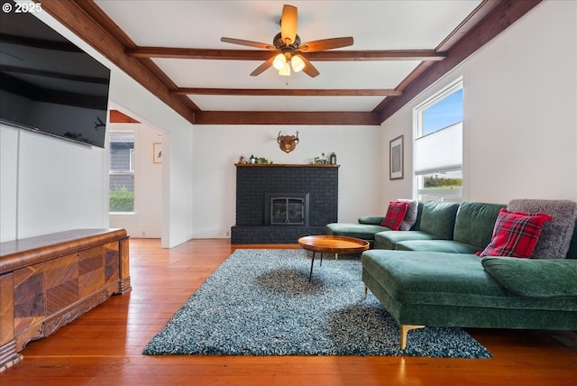 living area with wood-type flooring, a fireplace, a ceiling fan, and beamed ceiling