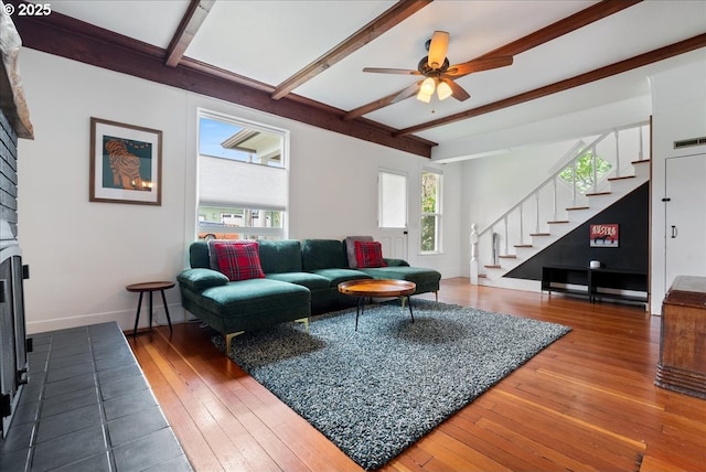 living area featuring stairs, a fireplace, hardwood / wood-style floors, and beamed ceiling