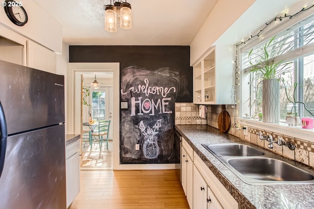 kitchen with sink, black fridge, light wood-type flooring, decorative backsplash, and white cabinets