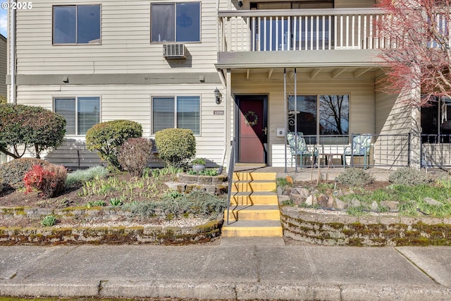 entrance to property with a wall unit AC, a balcony, and a porch