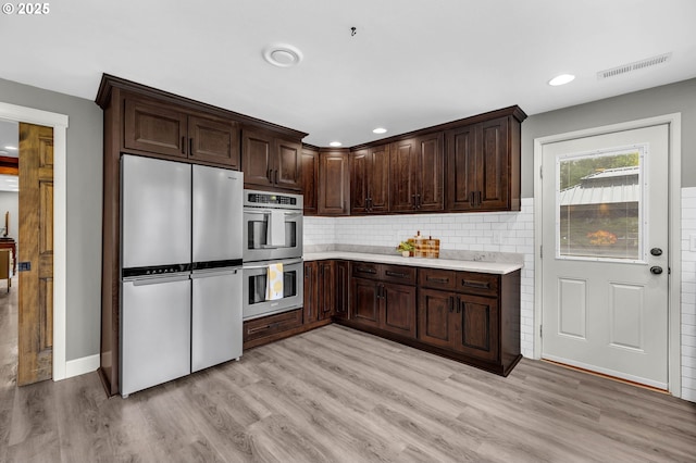 kitchen with light hardwood / wood-style flooring, backsplash, dark brown cabinets, and appliances with stainless steel finishes