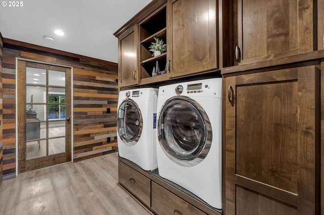 laundry room featuring cabinets, washing machine and clothes dryer, wooden walls, and light hardwood / wood-style flooring