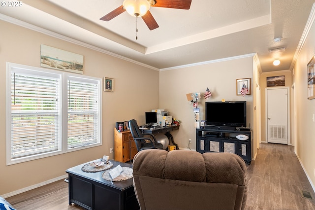 living room with a tray ceiling, wood finished floors, and ornamental molding