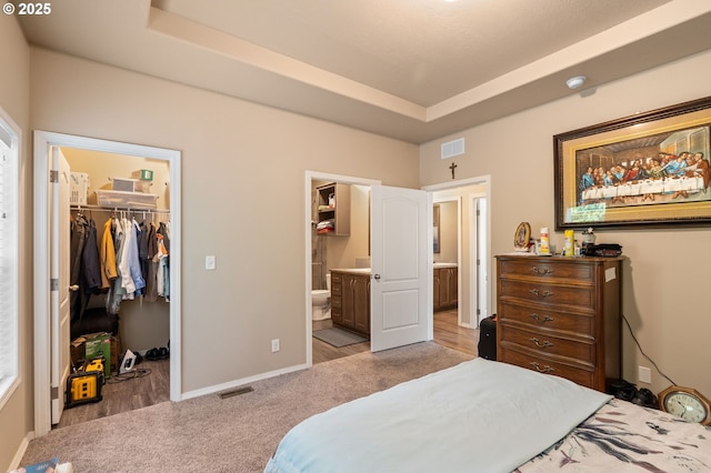 carpeted bedroom with a walk in closet, ensuite bath, a raised ceiling, and a closet