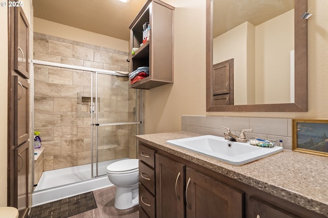 bathroom with toilet, vanity, a shower with door, hardwood / wood-style flooring, and decorative backsplash