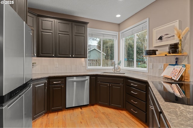 kitchen with a sink, appliances with stainless steel finishes, light wood finished floors, decorative backsplash, and light stone countertops