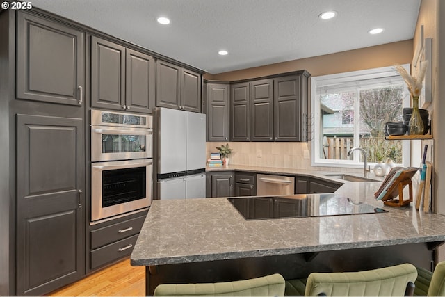 kitchen featuring gray cabinets, a sink, stainless steel appliances, a peninsula, and stone counters