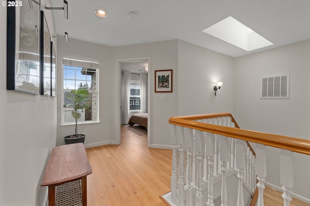 hall with an upstairs landing, visible vents, a skylight, and light wood-type flooring