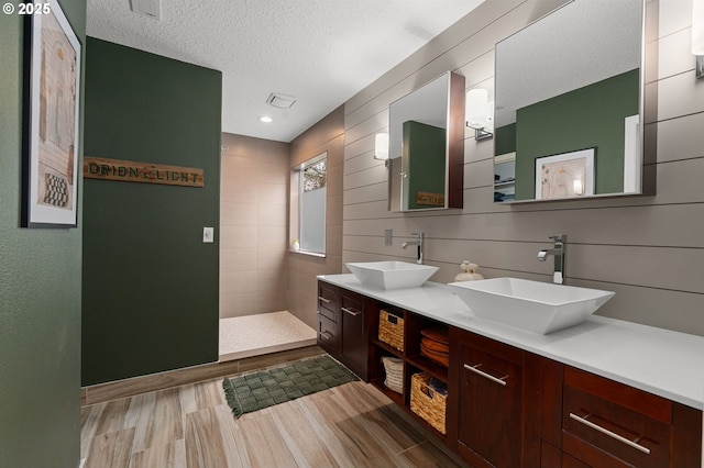 bathroom with double vanity, a walk in shower, a textured ceiling, and a sink