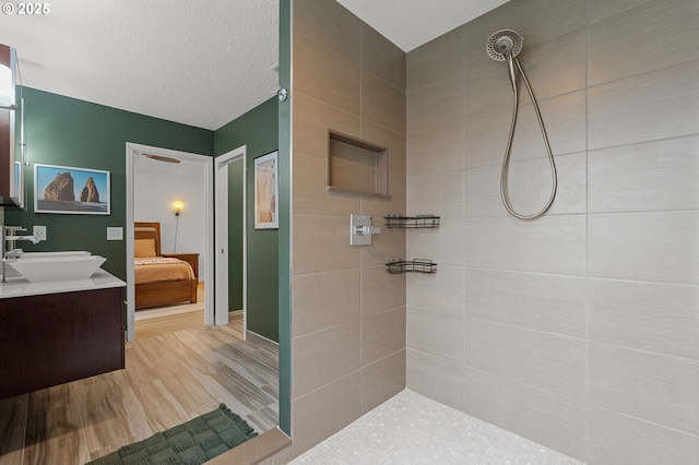 full bathroom with ensuite bathroom, a textured ceiling, wood finished floors, tiled shower, and vanity