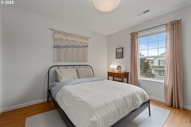 bedroom featuring visible vents, light wood-style flooring, a textured ceiling, and baseboards