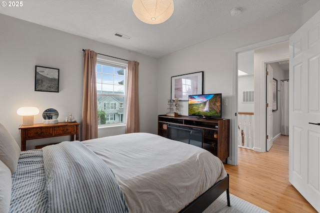 bedroom with a textured ceiling, baseboards, visible vents, and light wood-type flooring