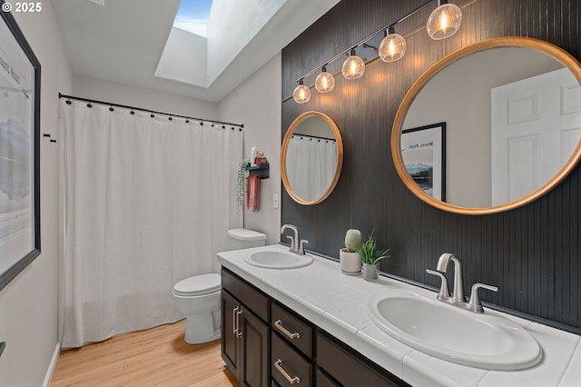 full bath with a skylight, toilet, wood finished floors, and a sink