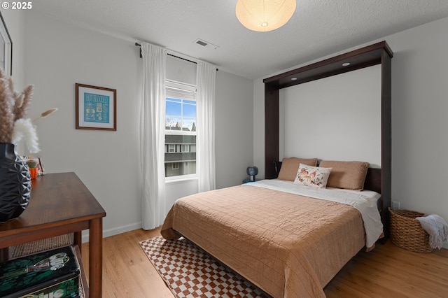 bedroom with baseboards, visible vents, light wood finished floors, and a textured ceiling