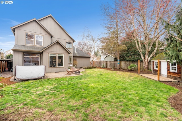 rear view of house featuring an outbuilding, a fenced backyard, a yard, roof with shingles, and a patio area