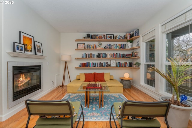 living area with baseboards, wood finished floors, and a tile fireplace