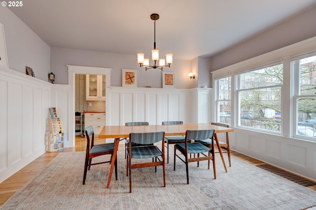 dining room featuring an inviting chandelier, a decorative wall, light wood-style floors, and visible vents